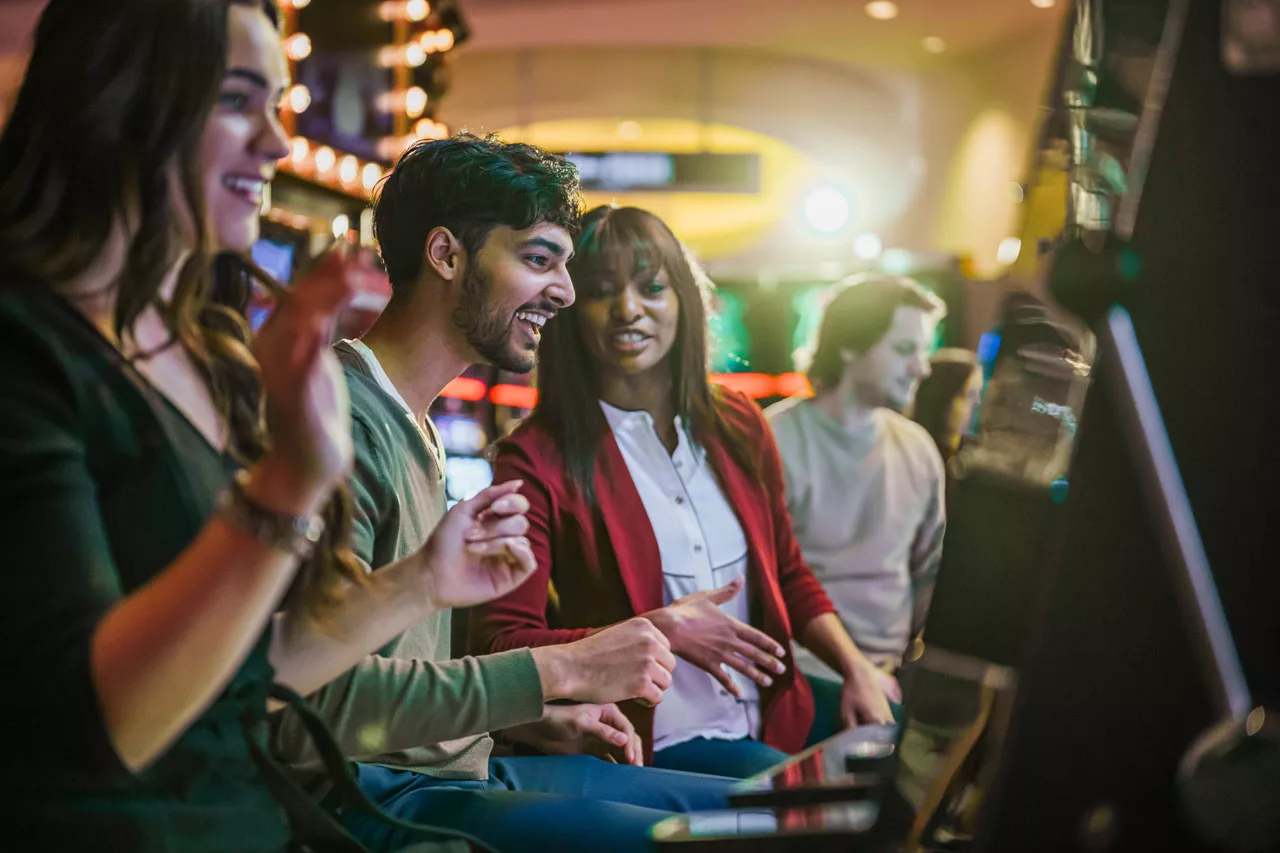 Young adults smiling and celebrating at slot machines.